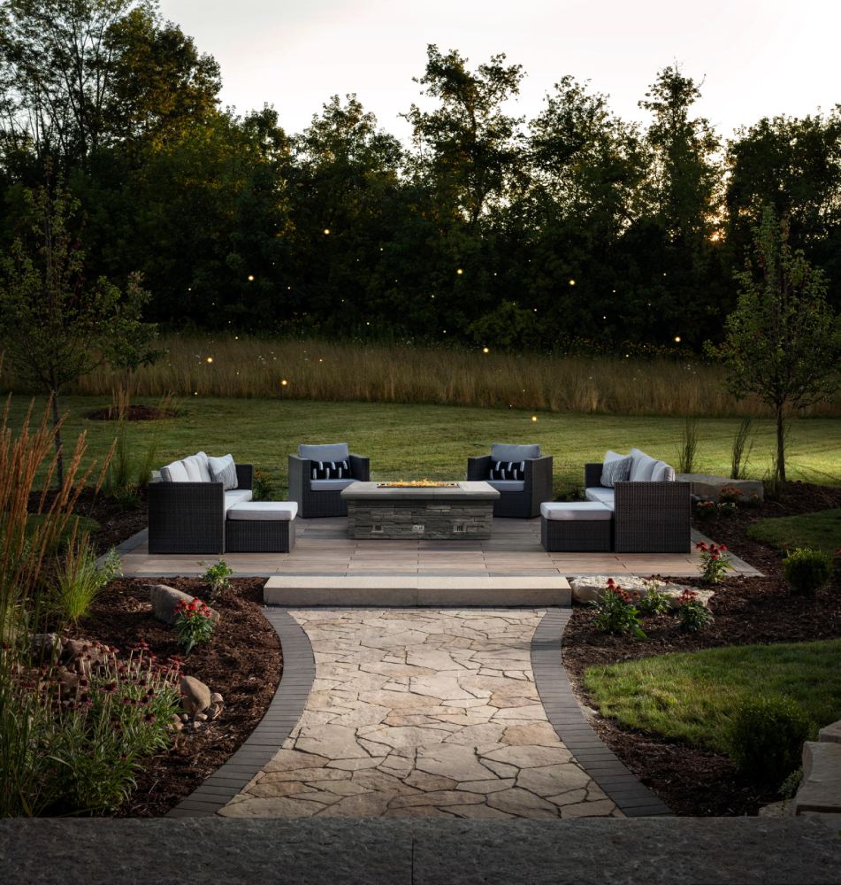 paved walkway with brown cushioned seating area and table with firepit